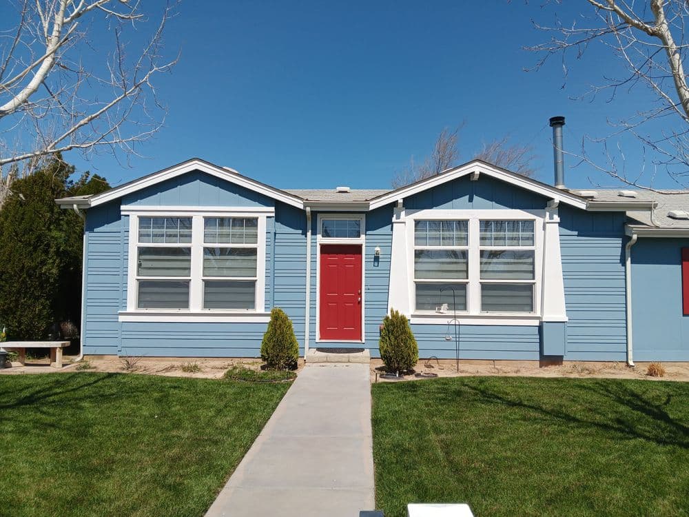 Blue house with red door, large windows, and a green yard under a clear sky.