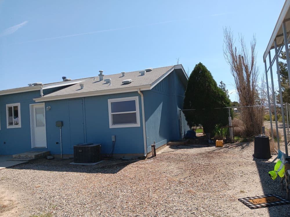 Blue residential house with a gray roof and fenced yard on a sunny day.