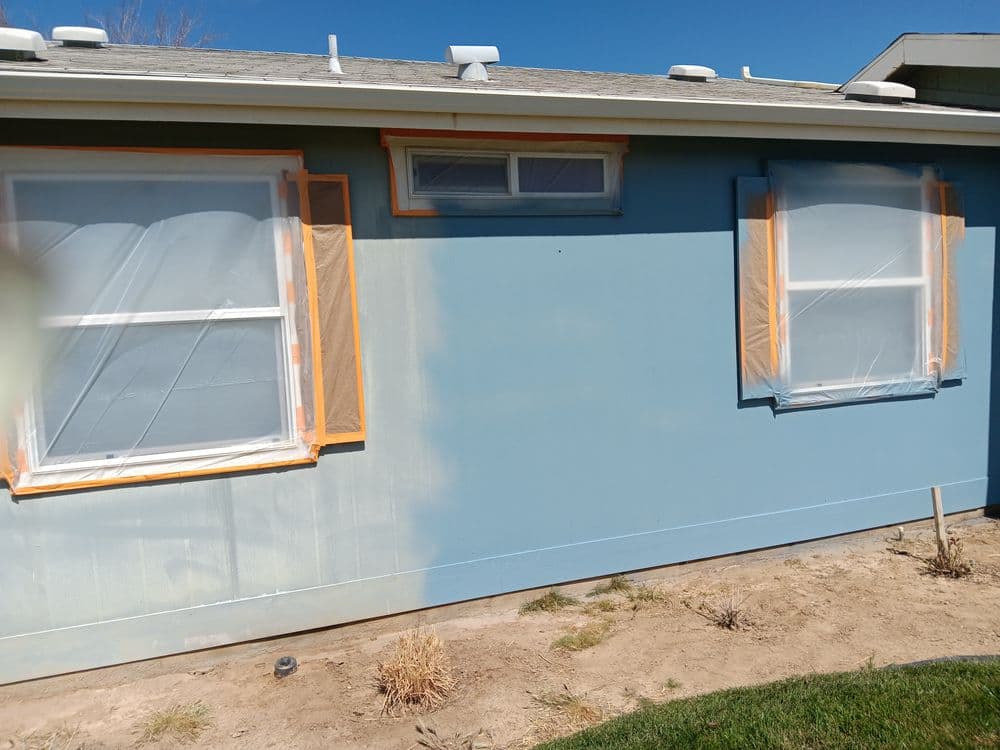 House exterior with blue paint, windows covered with plastic, and orange tape for renovation.
