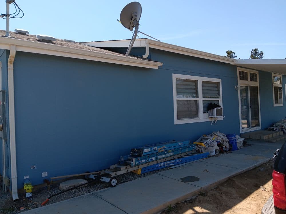 Blue house exterior with satellite dish, tools, and construction materials visible.