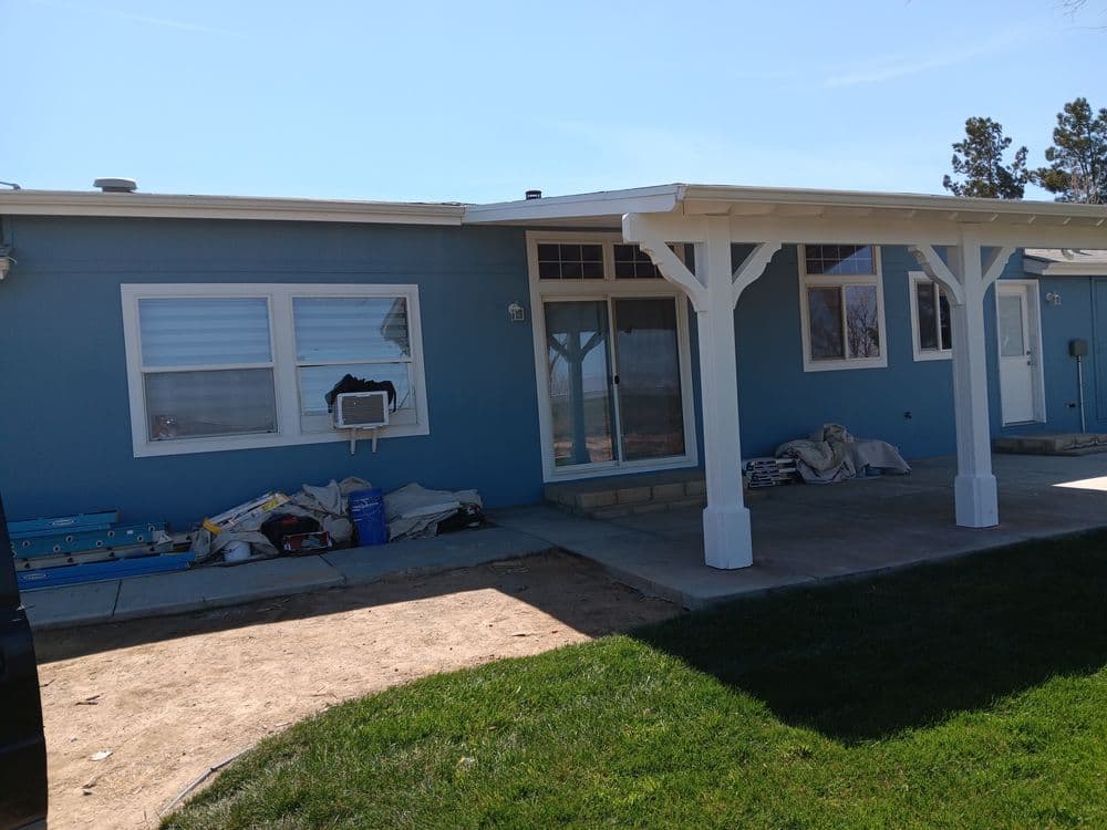 Blue house exterior with porch, unfinished landscaping, and construction materials visible.