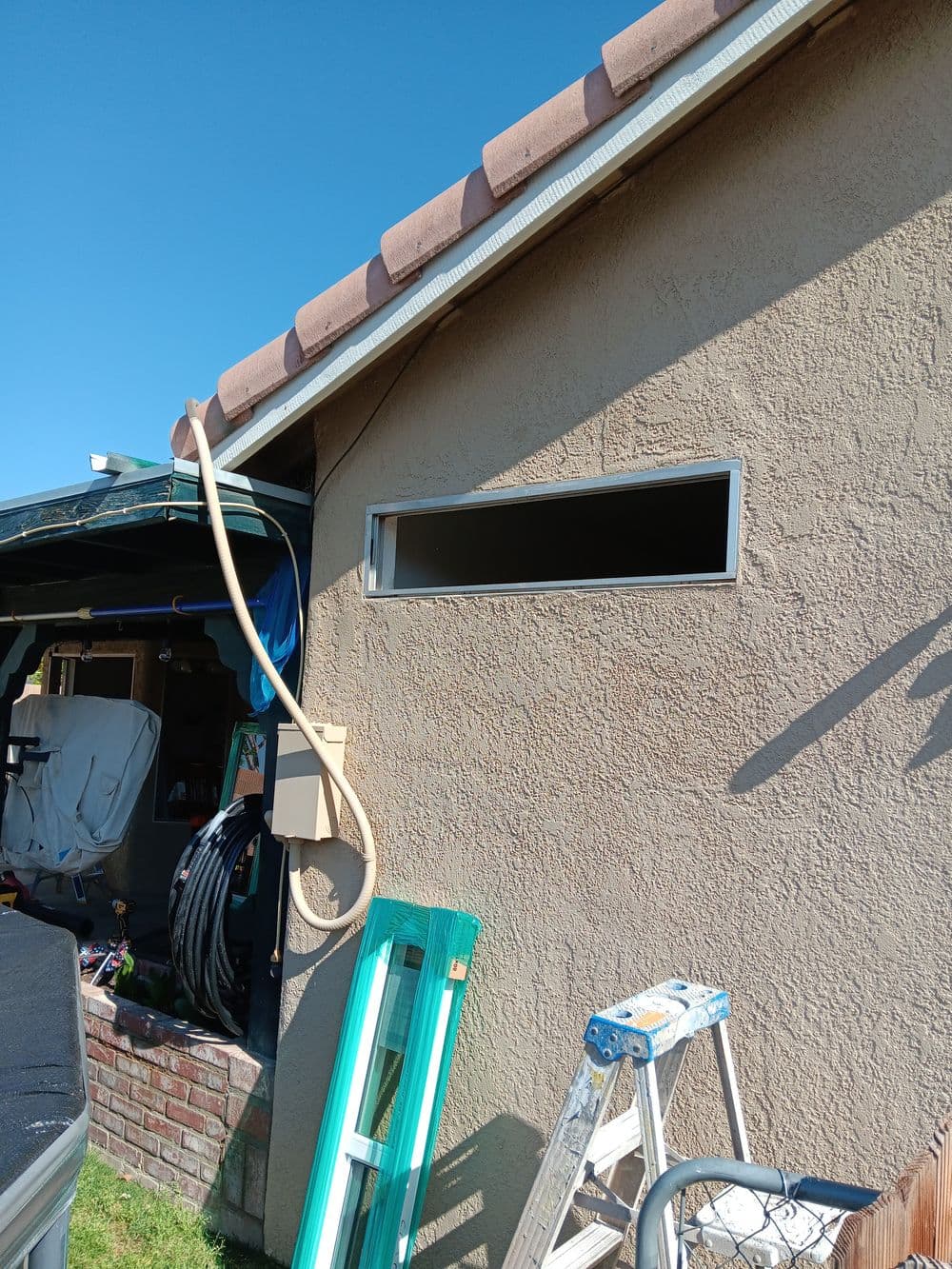 Side view of a home with an exterior wall, window, ladder, and tools in the yard.