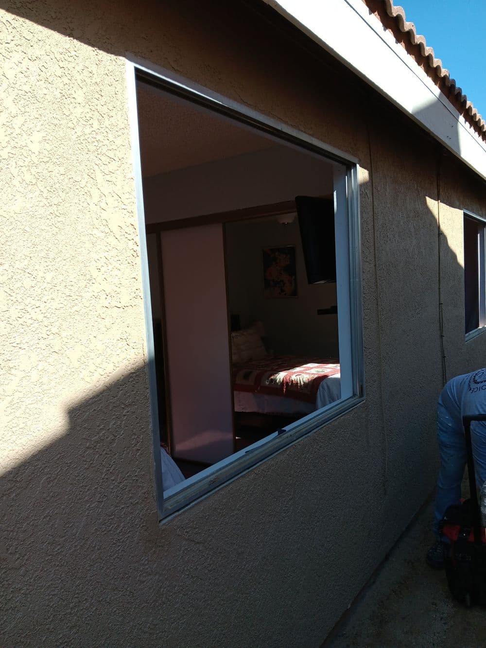 Window installation in a beige exterior wall showing a bedroom view inside.