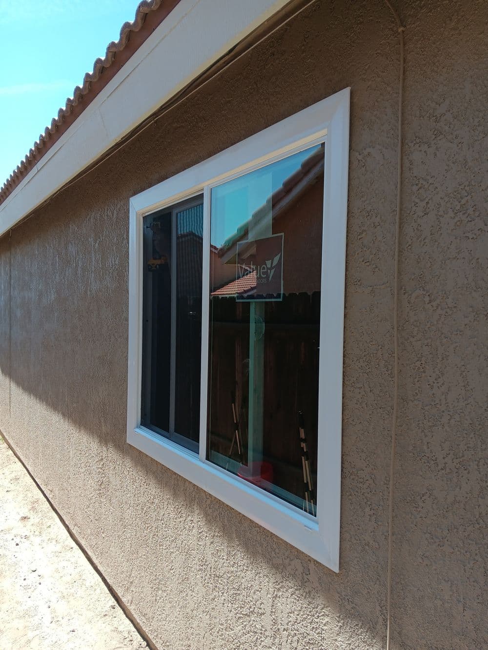 Modern window installation on textured beige wall of a house in bright sunlight.
