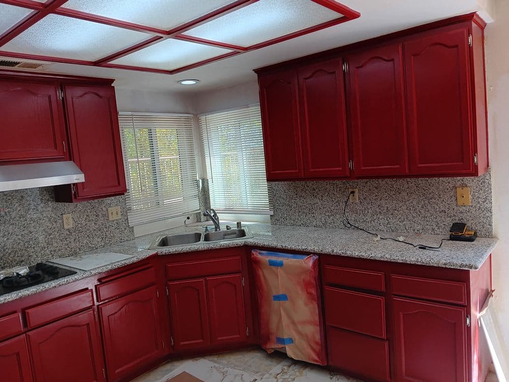 Red kitchen cabinets with granite countertops and a window, featuring a gas stove and sink.