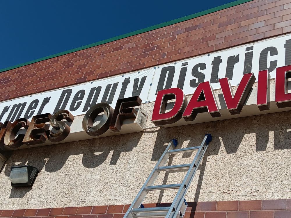 Sign installation for "Offices of David" on a brick building with a clear blue sky.