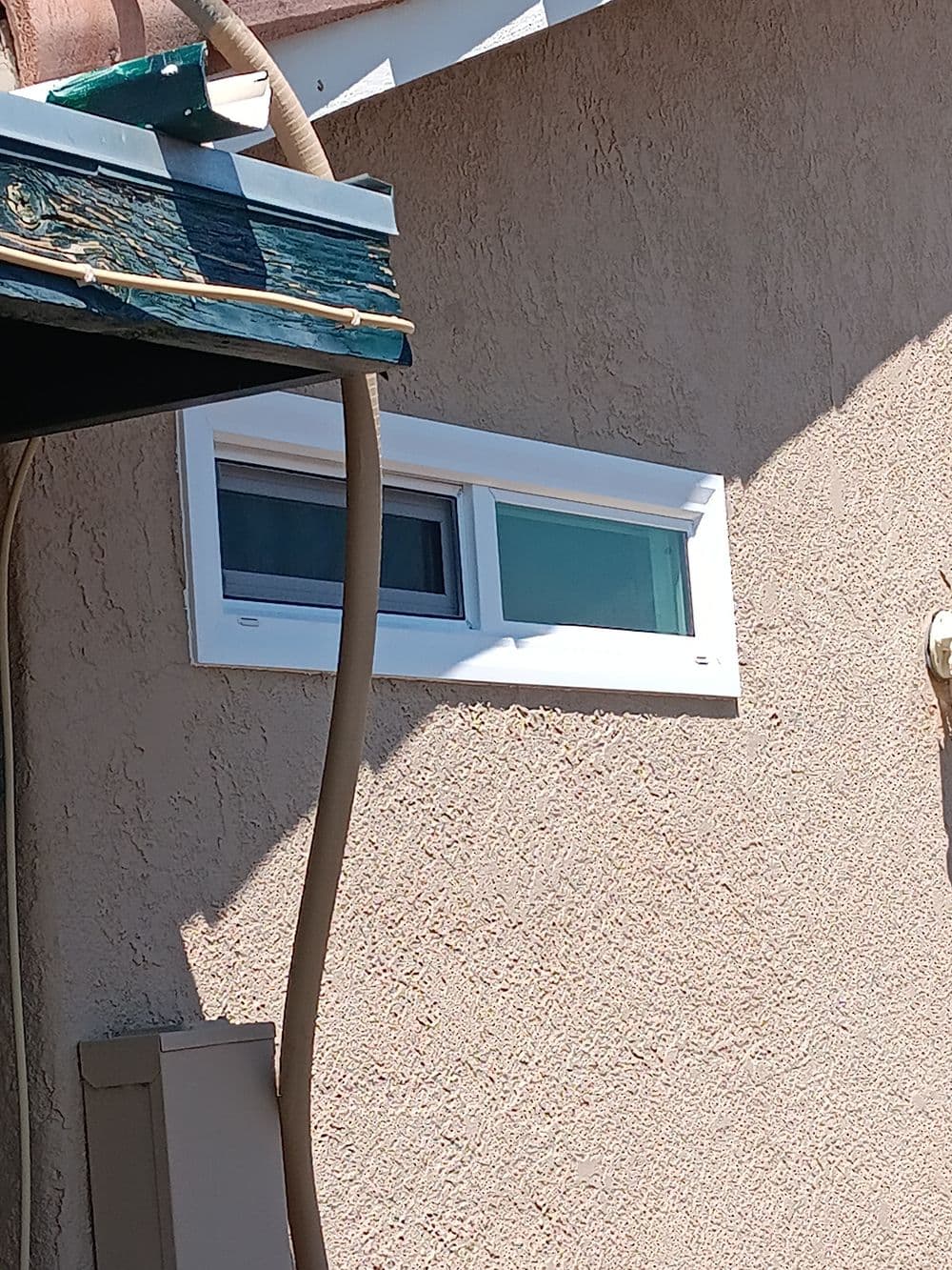 Modern window installation on a textured exterior wall with visible sunlight.