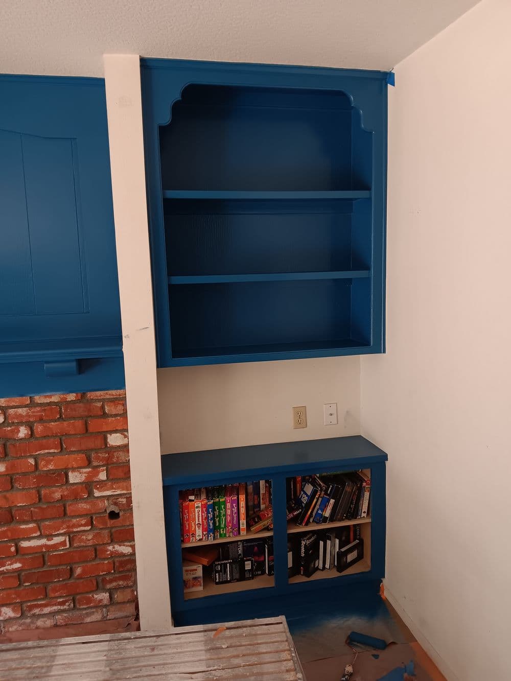 Blue bookshelf with open shelves and closed storage, featuring a brick accent wall.