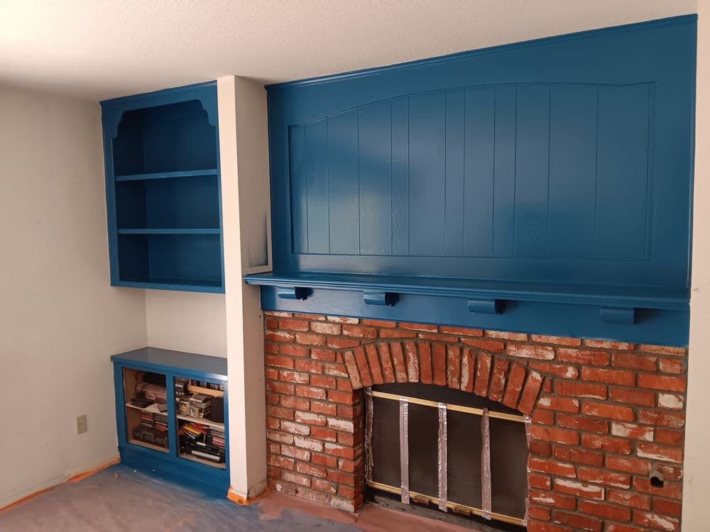 Blue-painted living room fireplace and built-in shelves with brick accents.