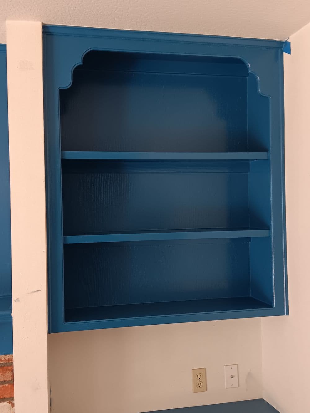 Blue painted open shelving unit with decorative arch on top and three empty shelves.