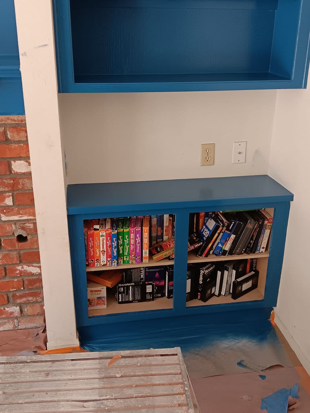 Blue bookshelf with colorful books and games, featuring a painted wall and brick accents.
