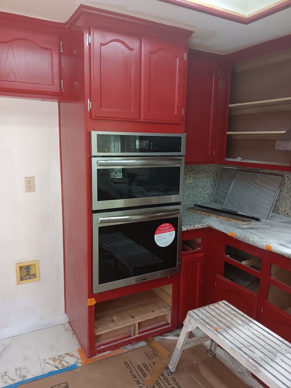 Modern kitchen renovation featuring red cabinetry and stainless steel double ovens.