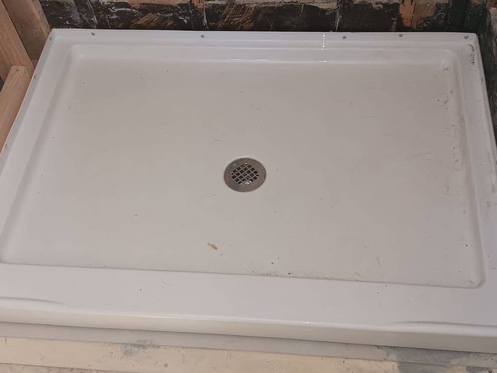 White shower base with a drain in the center, set on a construction site background.