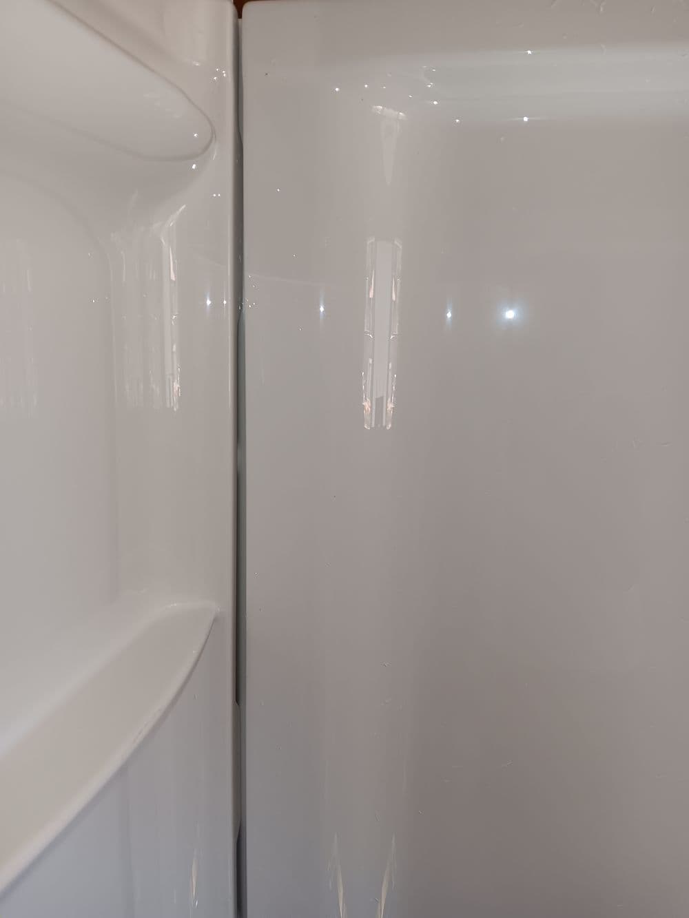 Close-up of a clean, shiny refrigerator interior with bright lighting and smooth surfaces.