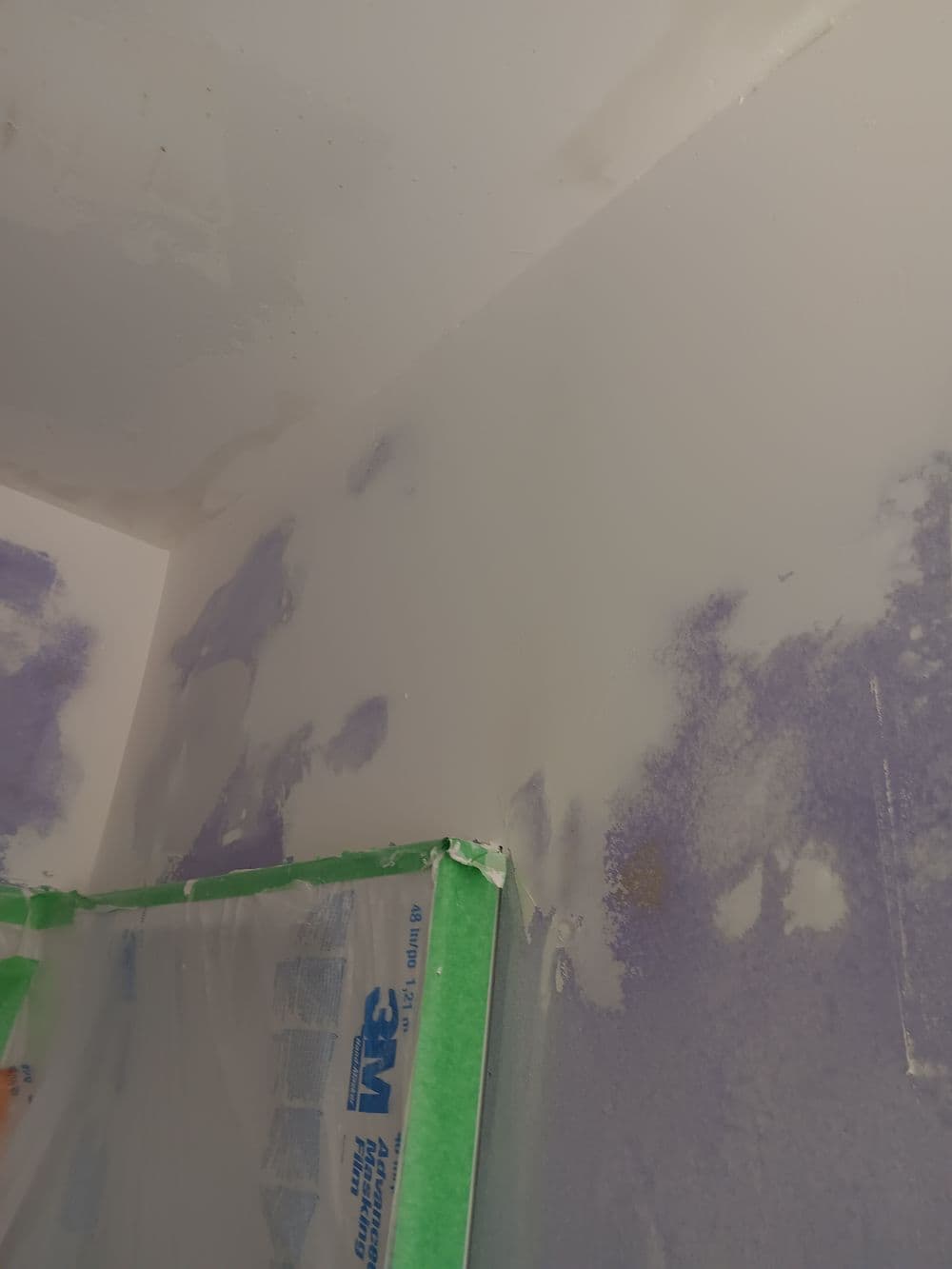 Close-up of a partially painted wall with purple patches and green painter's tape.