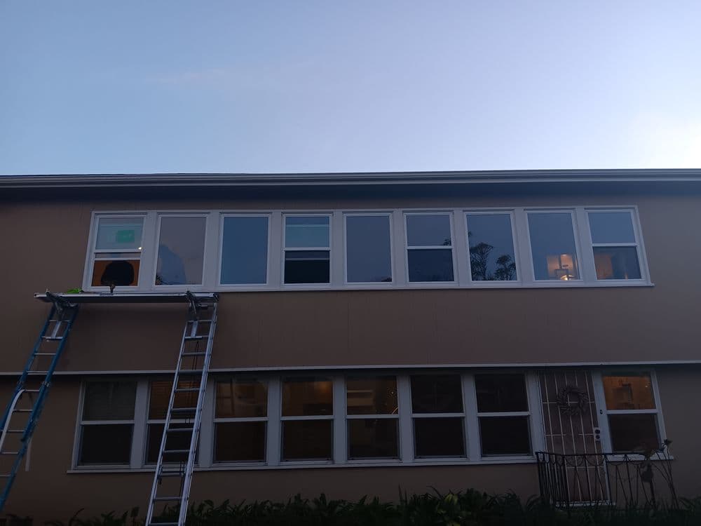 Two-story residential building with new windows, ladder leaning against exterior wall.