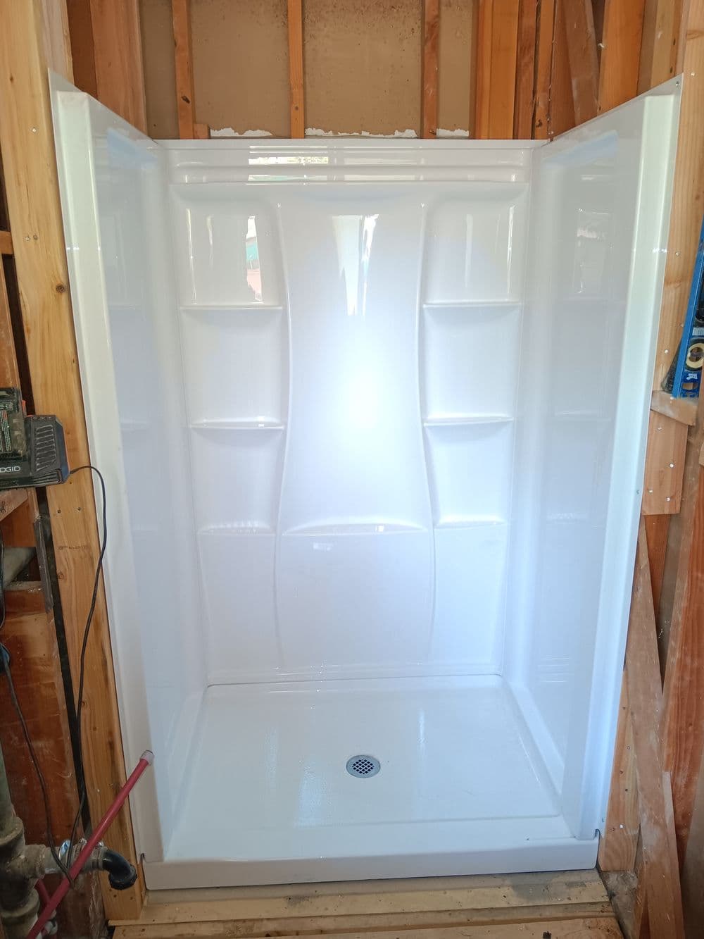New white shower stall installed in a bathroom renovation, showcasing built-in shelving.