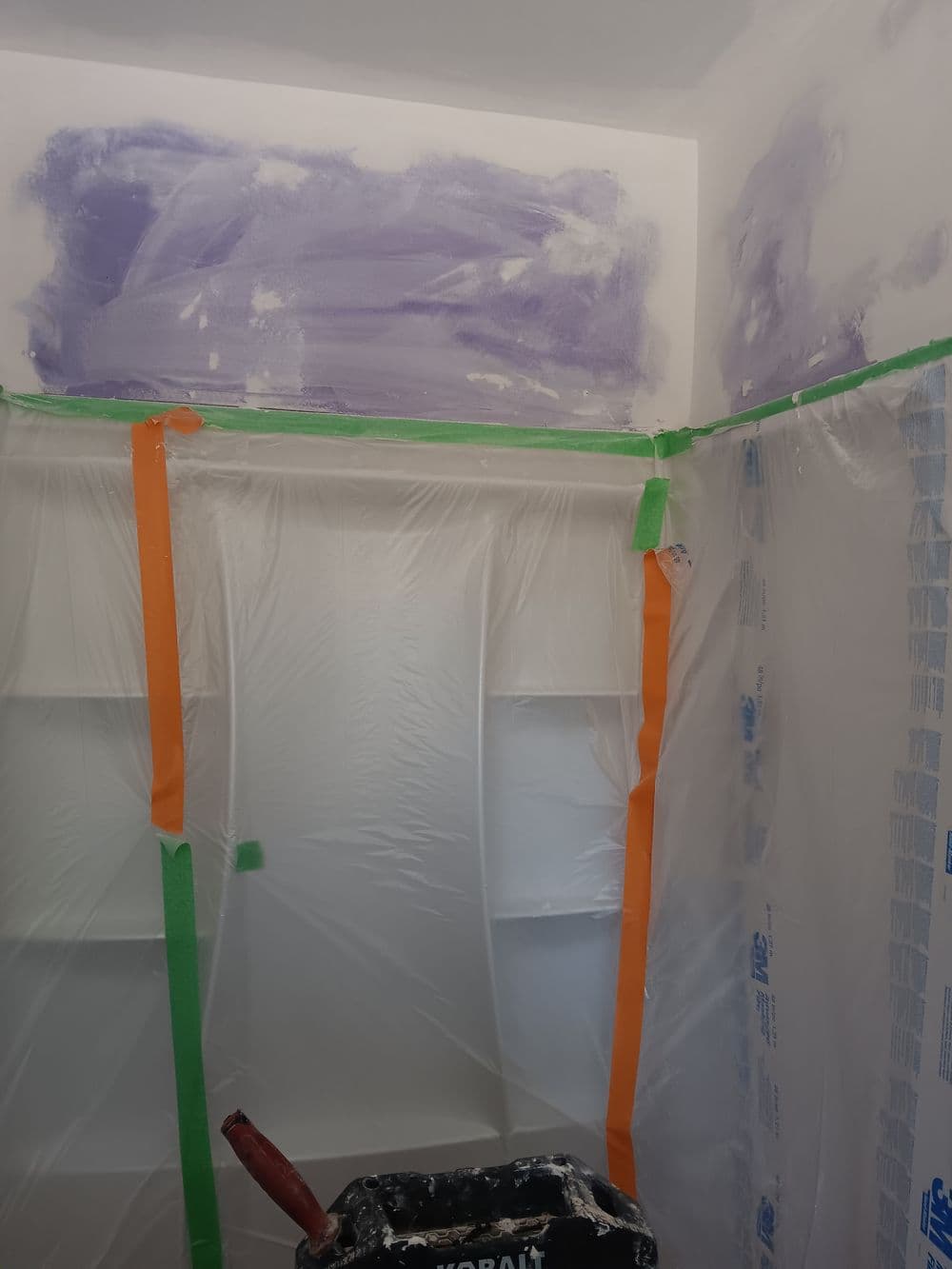 Room being painted with protective plastic covering, purple paint on the walls and green tape.