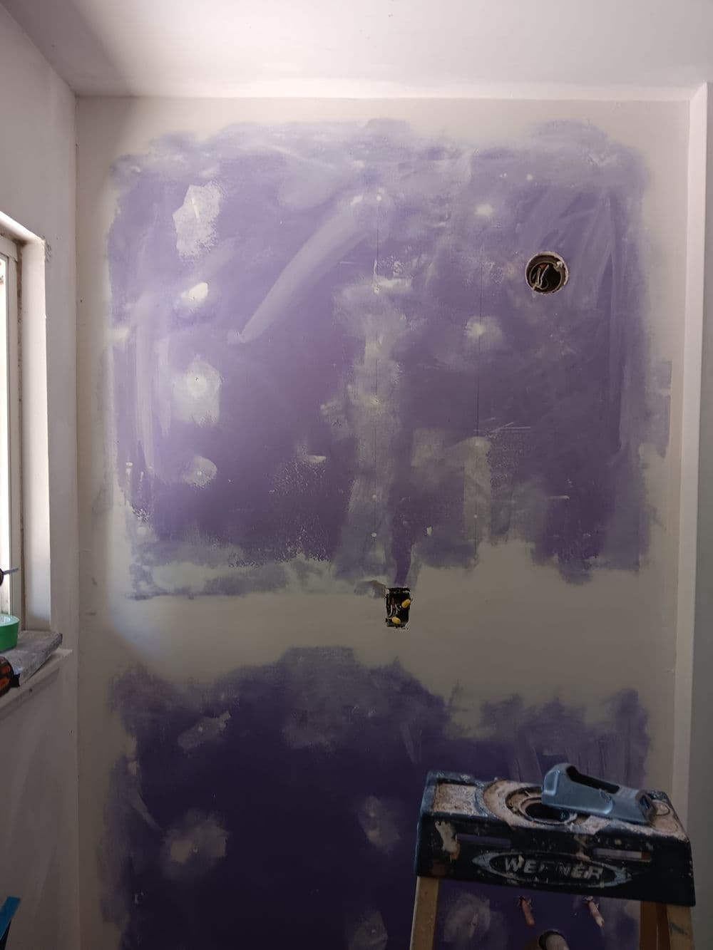 Wall undergoing renovation with purple primer, holes for fixtures, and a workbench in view.