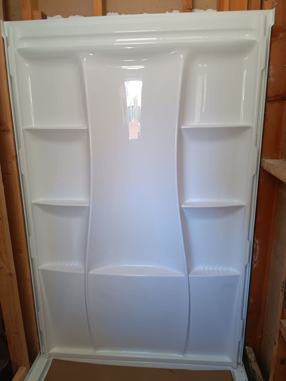 White acrylic shower wall with built-in shelves in a framed construction setting.