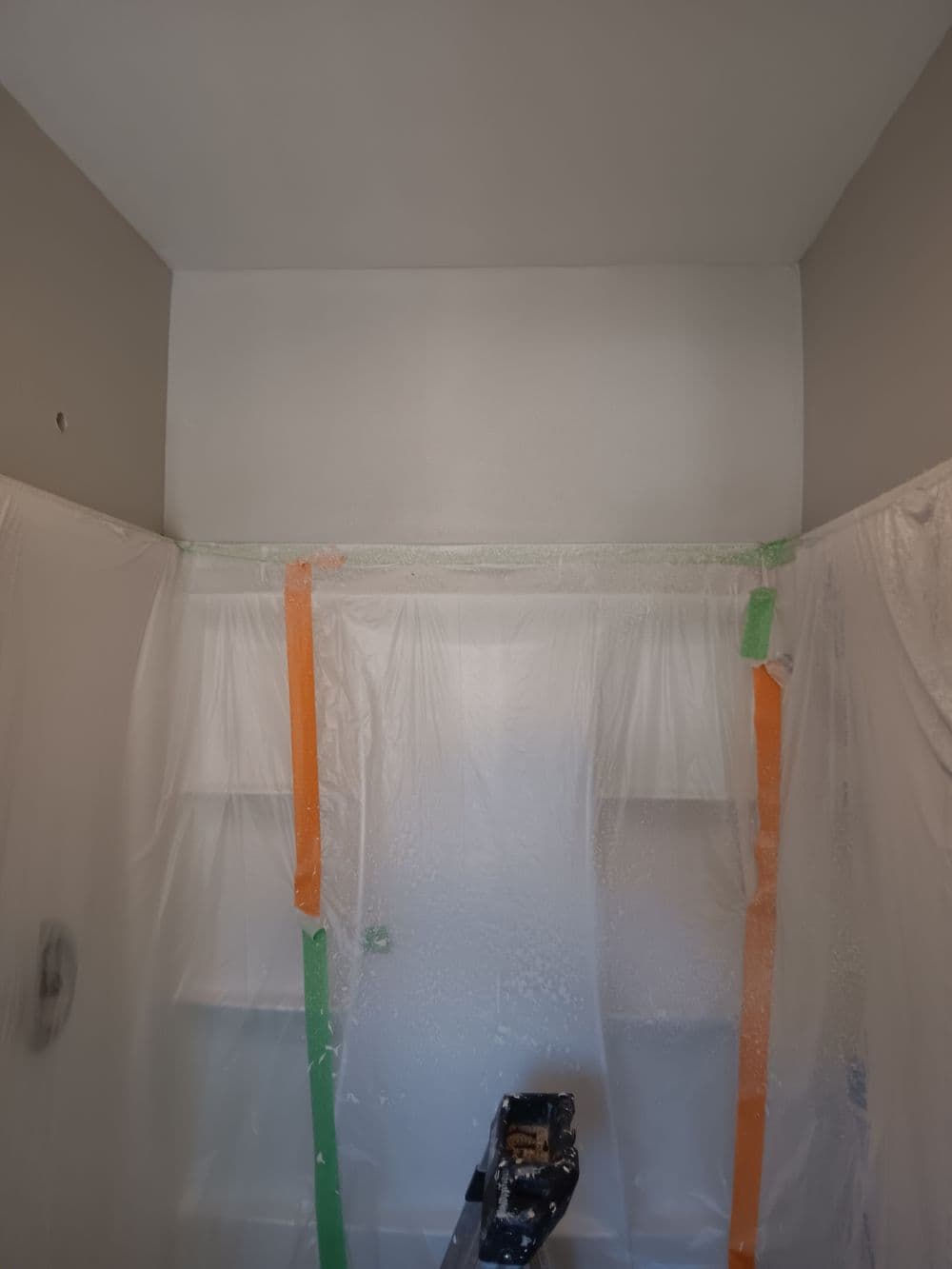 Bathroom renovation progress with protective plastic sheeting and spray equipment in view.