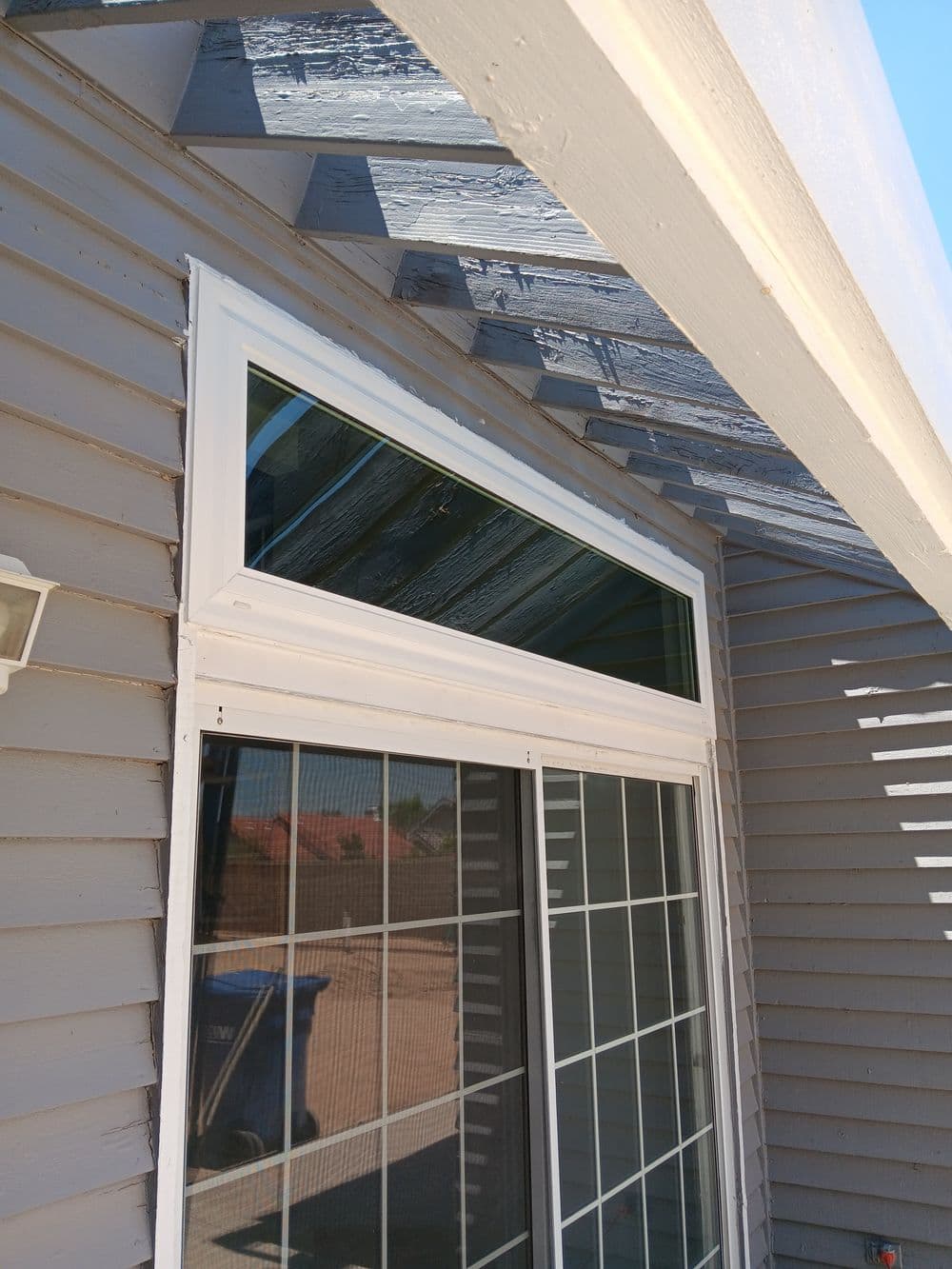White framed window installation on a gray house exterior with a sloped roof.