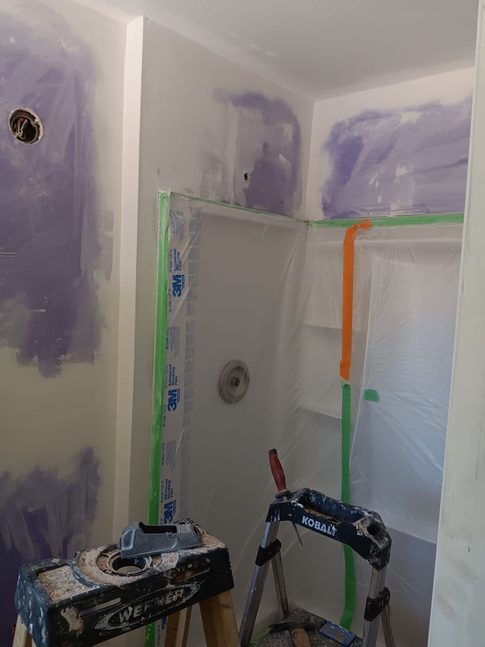Renovation of a shower area with drywall patching, protective sheeting, and a ladder.
