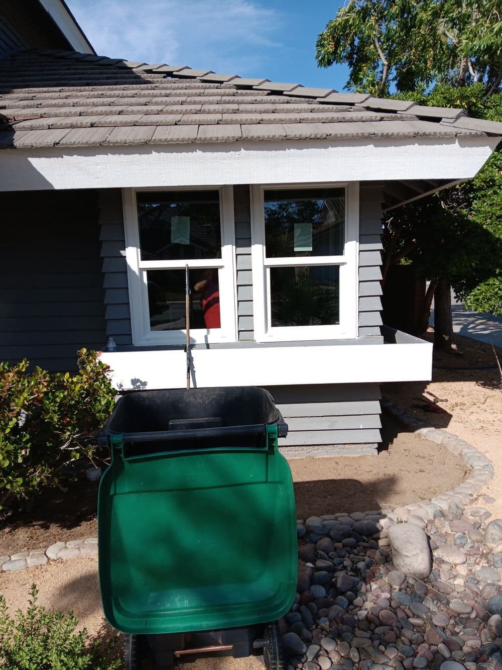 Green garden cart in front of house with gray siding and windows on a sunny day.