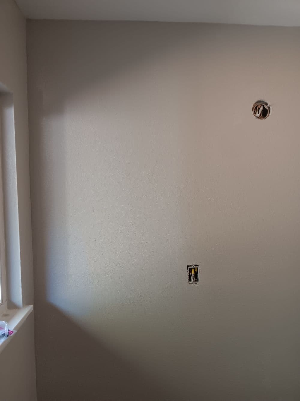 Interior wall with light switch and outlet openings, freshly painted in neutral color.