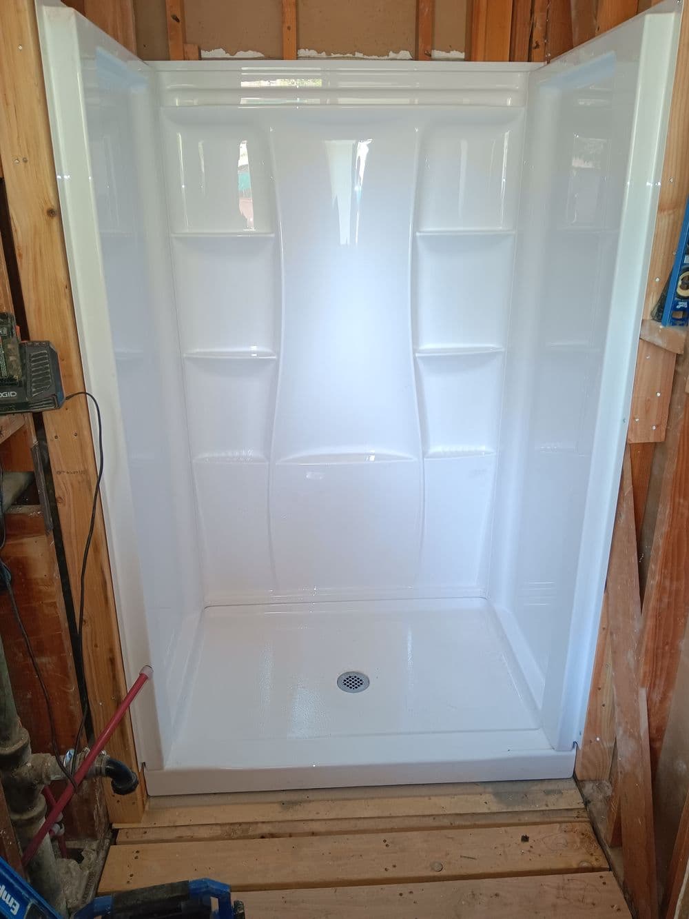 New white shower stall installed in a wooden-framed bathroom renovation.