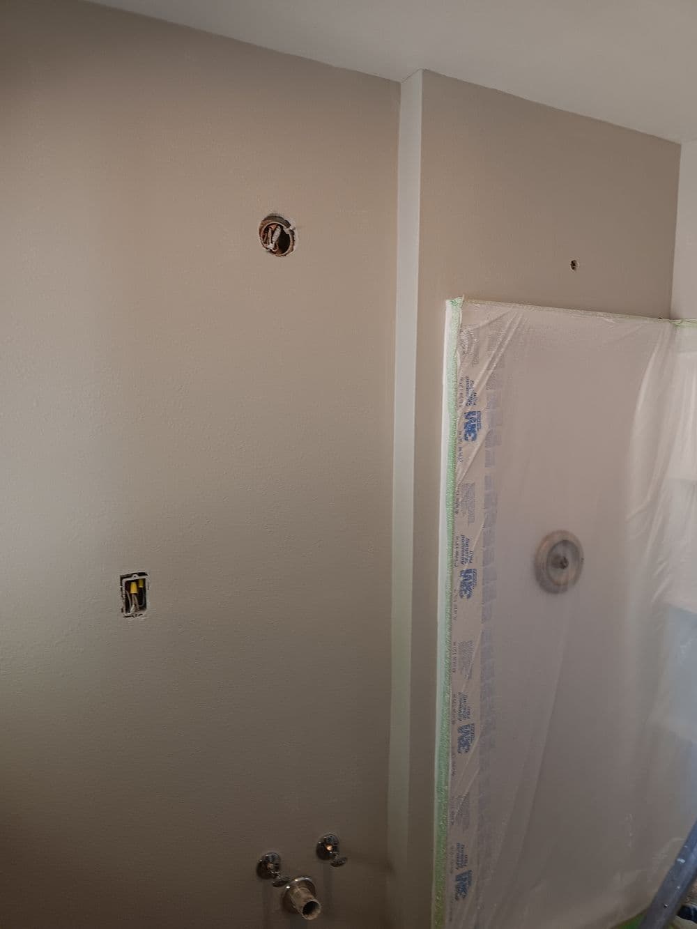 Bathroom renovation progress featuring newly primed wall and shower area taped for painting.