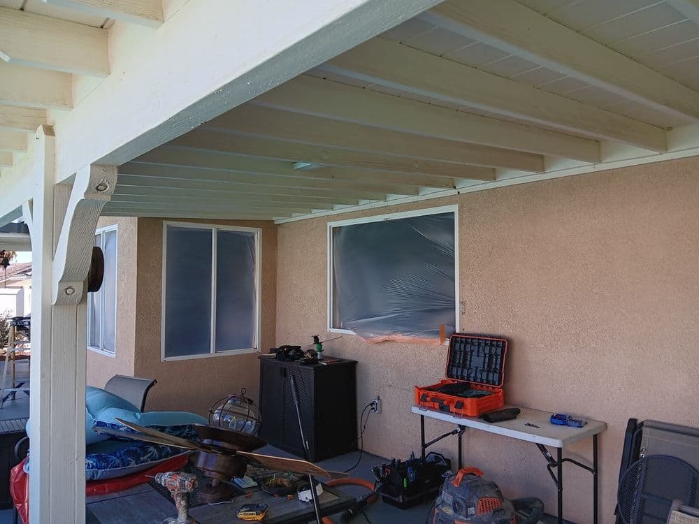 Renovated patio with plastic-covered windows and construction tools on a table.