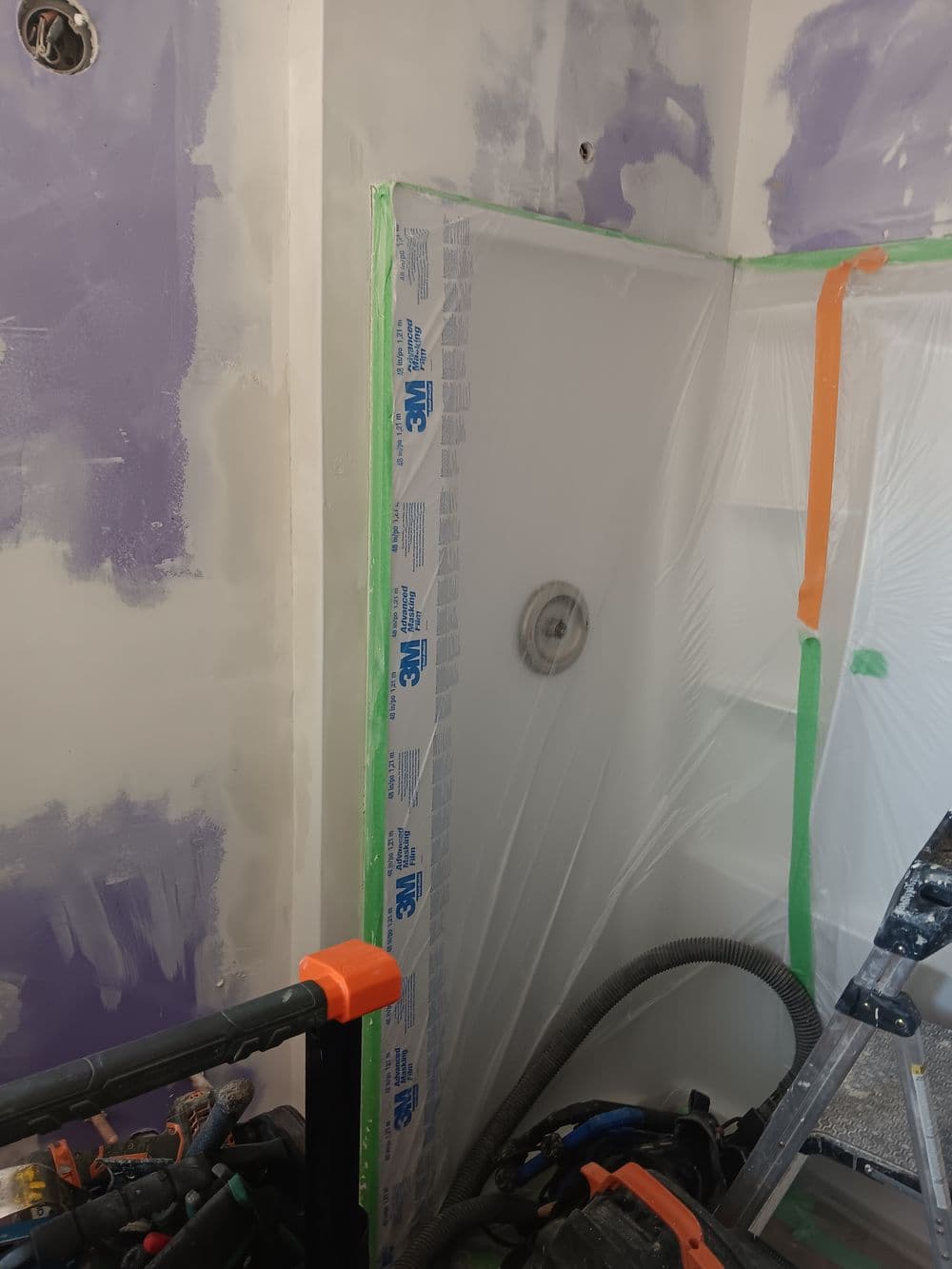 Shower renovation with plastic sheeting and tools, freshly painted purple walls.