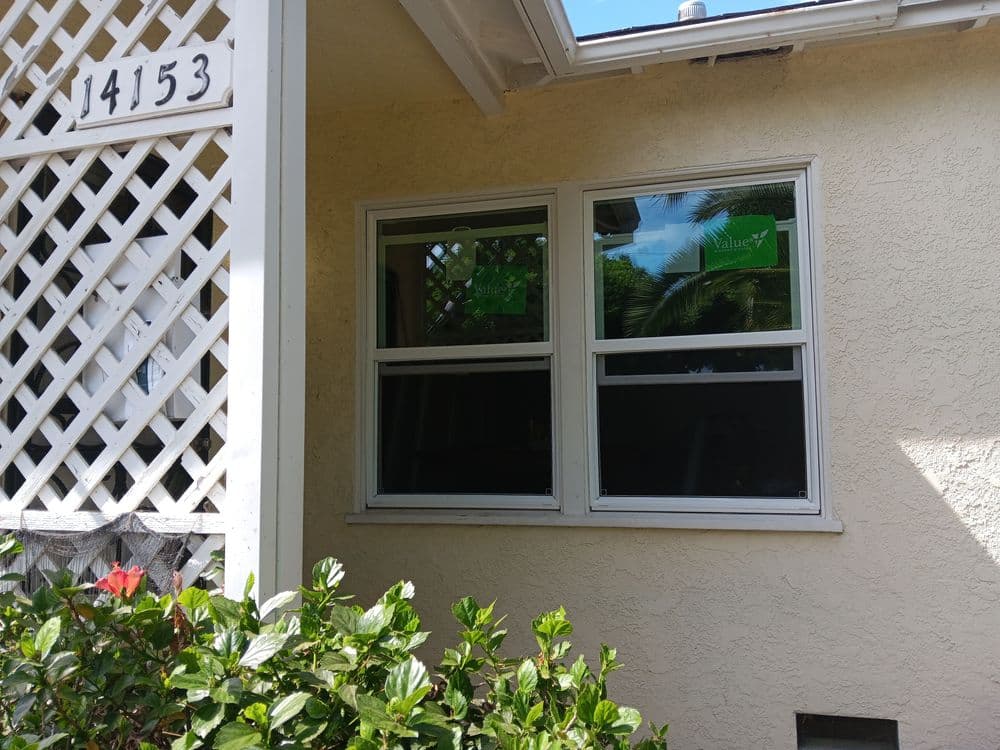 Exterior view of a house with white framed windows and green plants in the foreground.