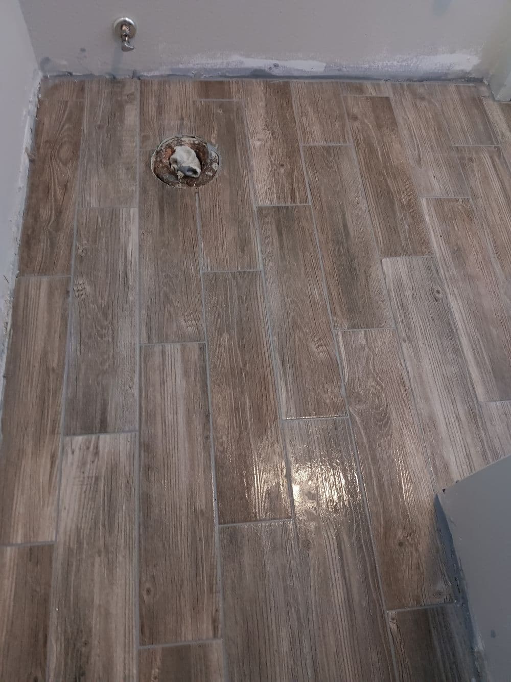 Newly installed wood-look tile flooring in a bathroom, showcasing a drainage hole.