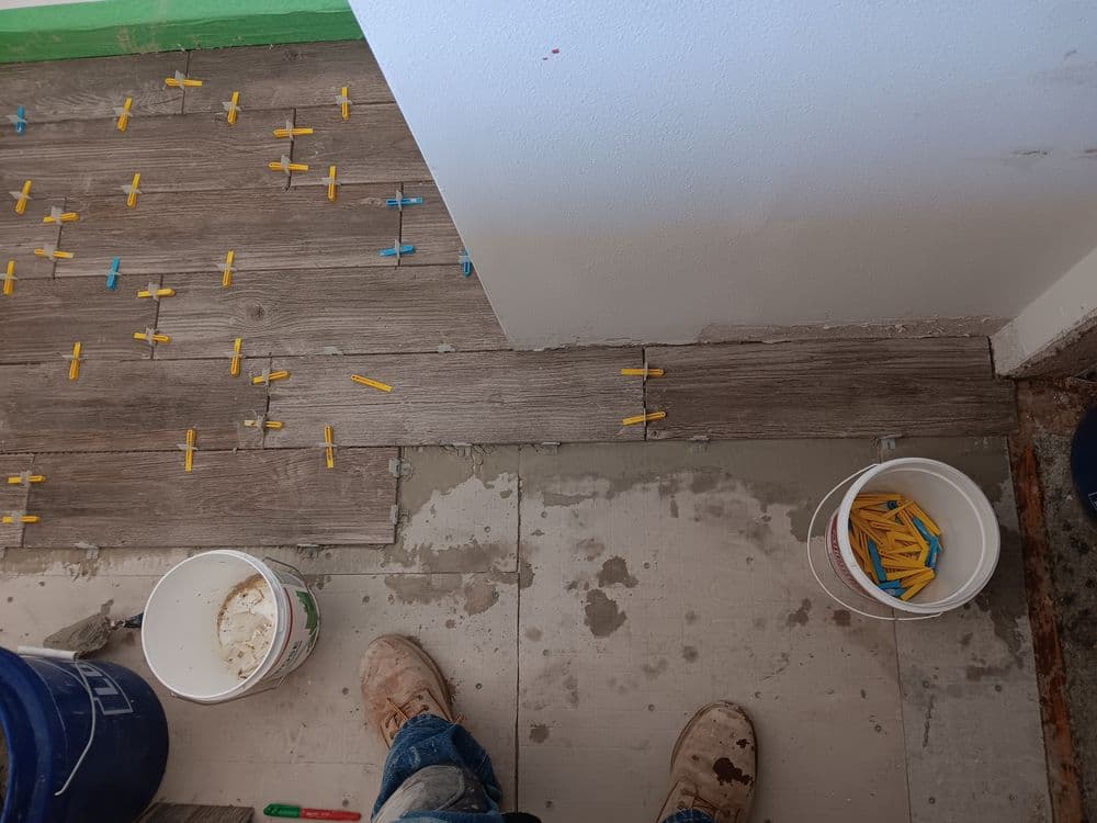 Floor tiling process with spacers, buckets, and tools in a room under renovation.