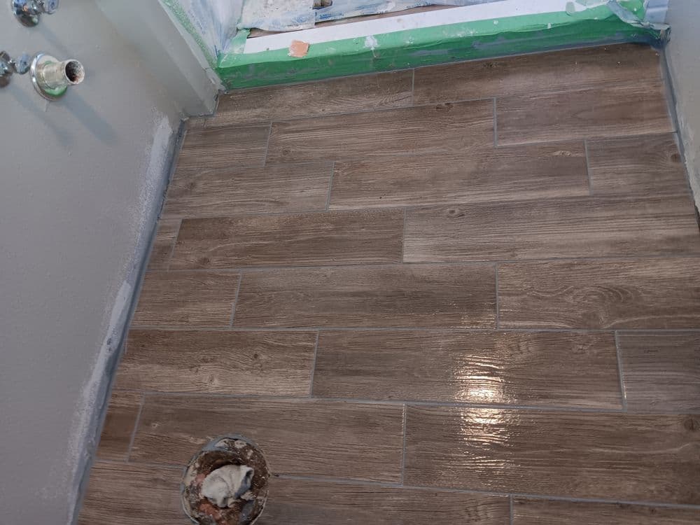 Newly installed wooden tile flooring in a bathroom with plumbing access hole visible.