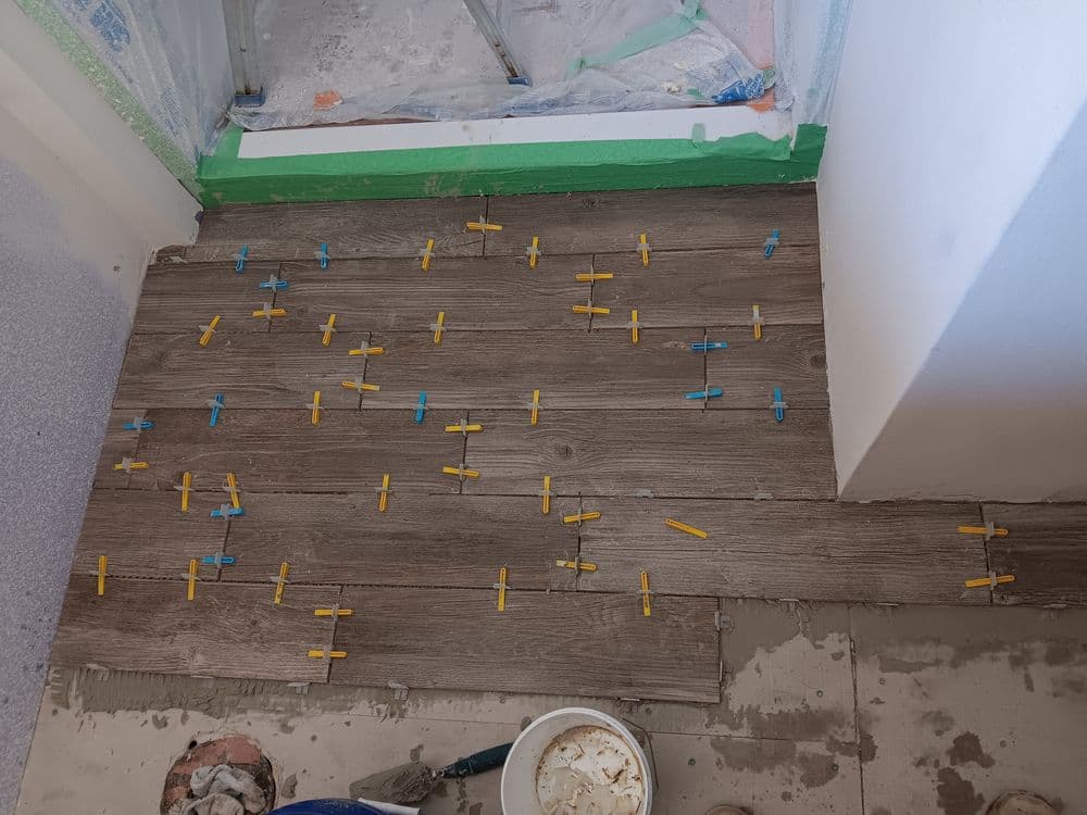 Tile installation process with leveling spacers on a wooden floor in a partially renovated room.