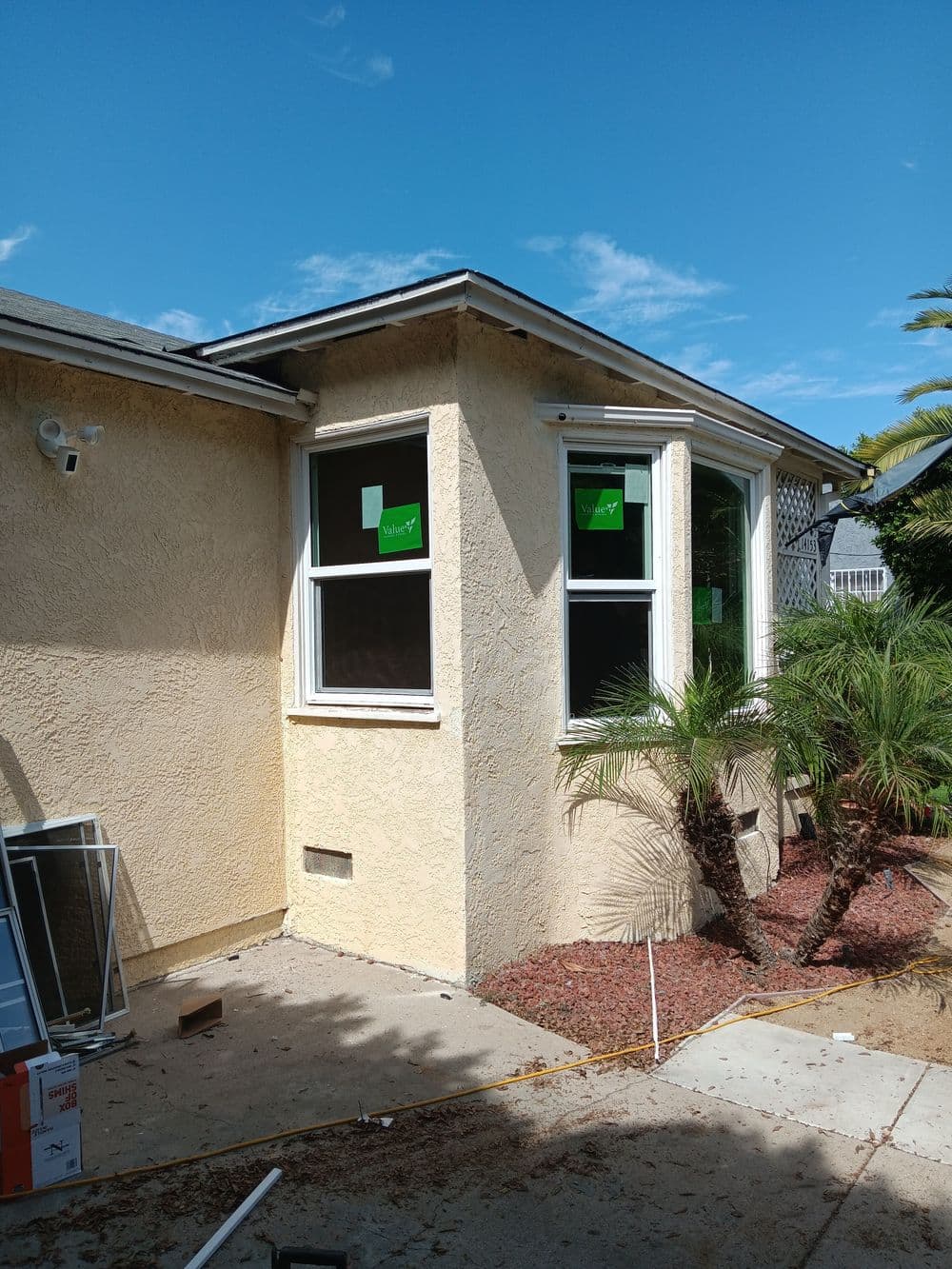 Two-story house corner with new windows, palm trees, and clear blue sky.
