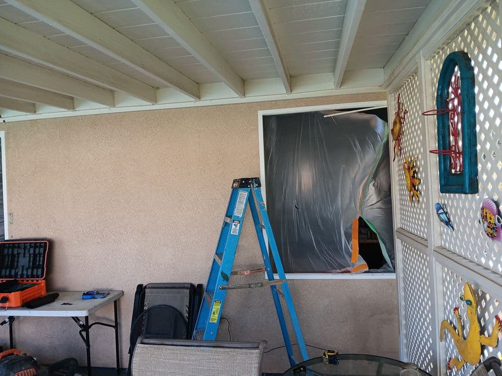 Blue ladder next to a covered window and construction tools on a patio.