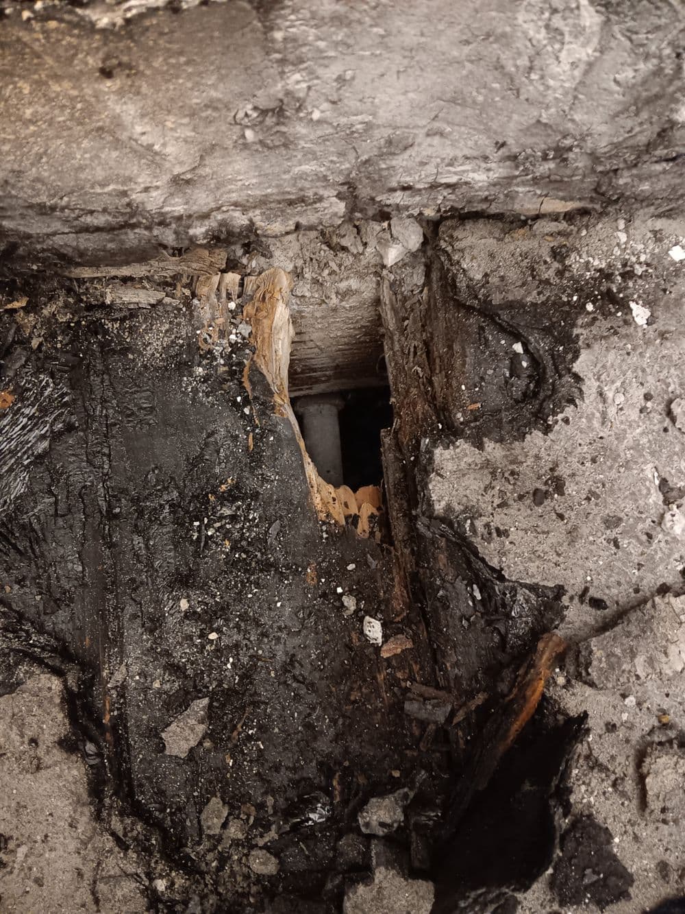 Damaged wood with visible cracks and darkened areas near a hidden pipe opening.