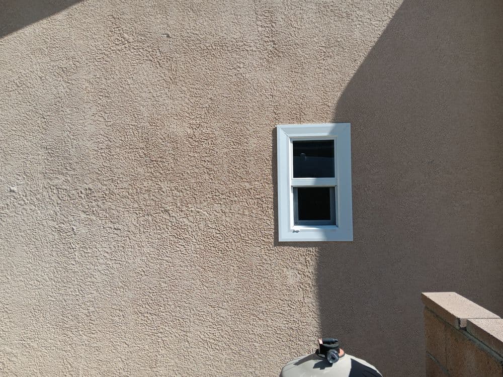 Exterior wall with textured beige finish and a small white window.